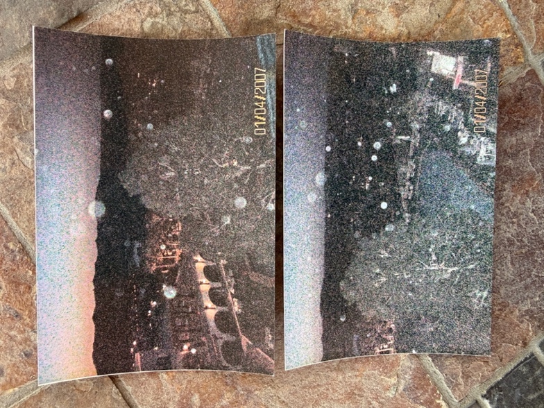 Two printed night photographs lying side by side on a stone surface, with small round lights visible.