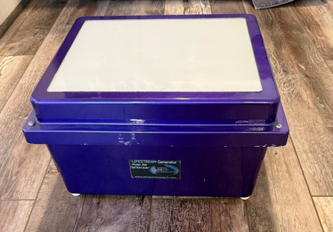 A purple rectangular Life Stream Generator case with a cream top on a wooden floor.